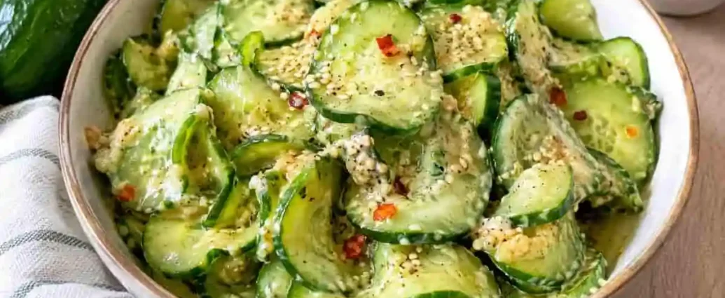 Insalata di cetrioli condita con salsa cremosa, semi di sesamo e fiocchi di peperoncino servita in una ciotola di ceramica chiara.