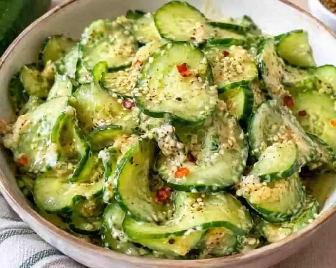 Insalata di cetrioli condita con salsa cremosa, semi di sesamo e fiocchi di peperoncino servita in una ciotola di ceramica chiara.